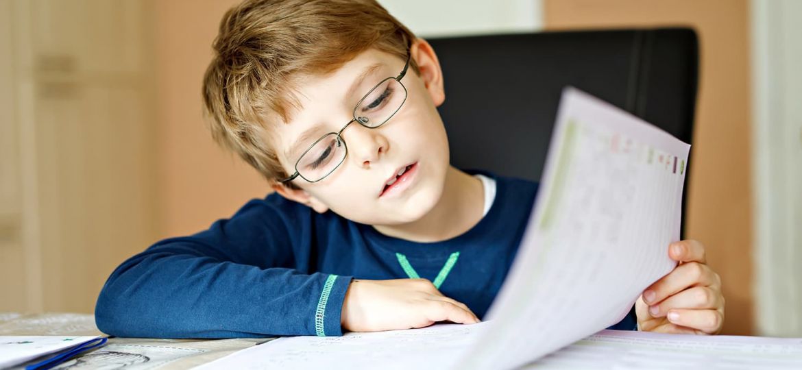 child with glasses sitting at desk doing school work