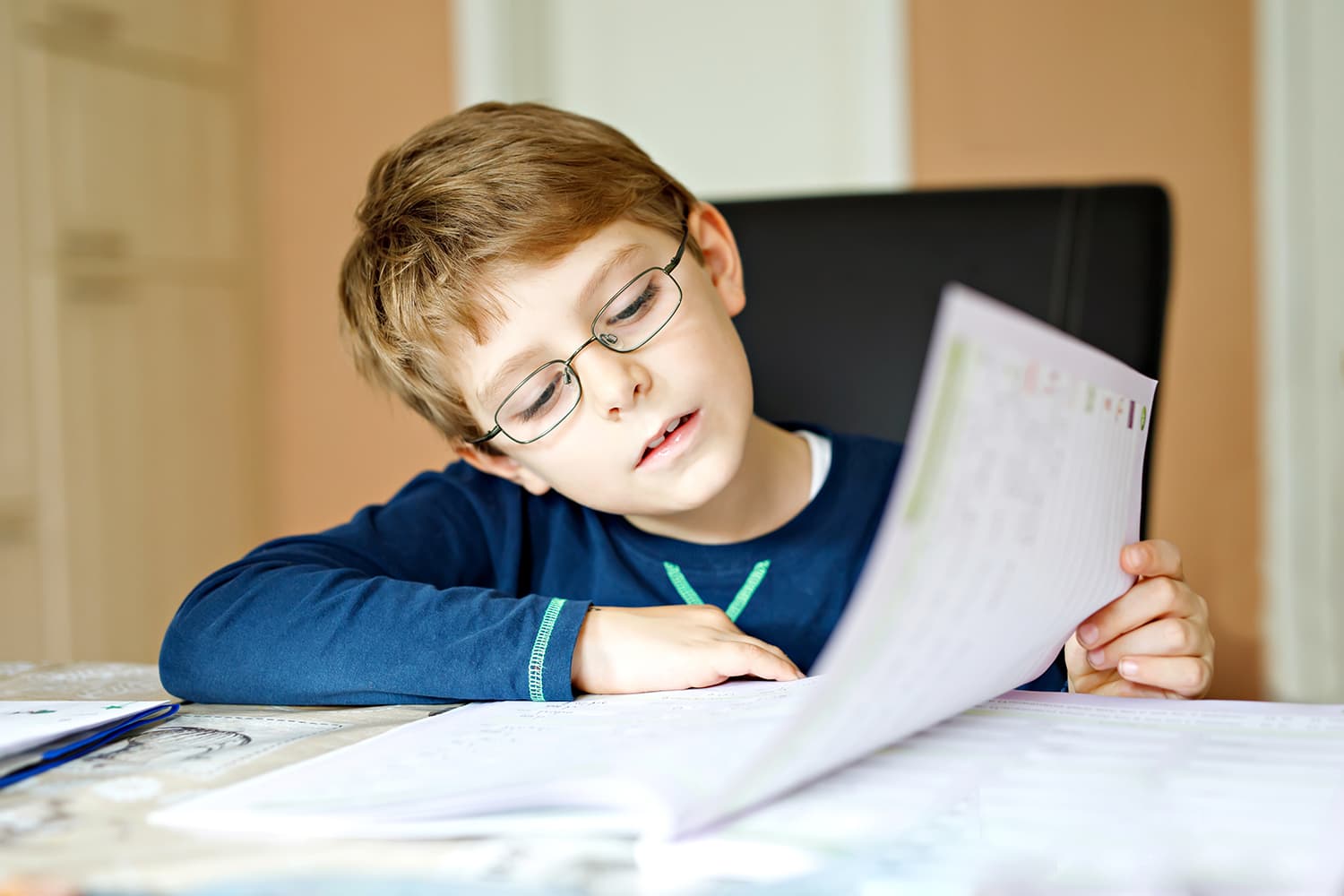 child with glasses sitting at desk doing school work